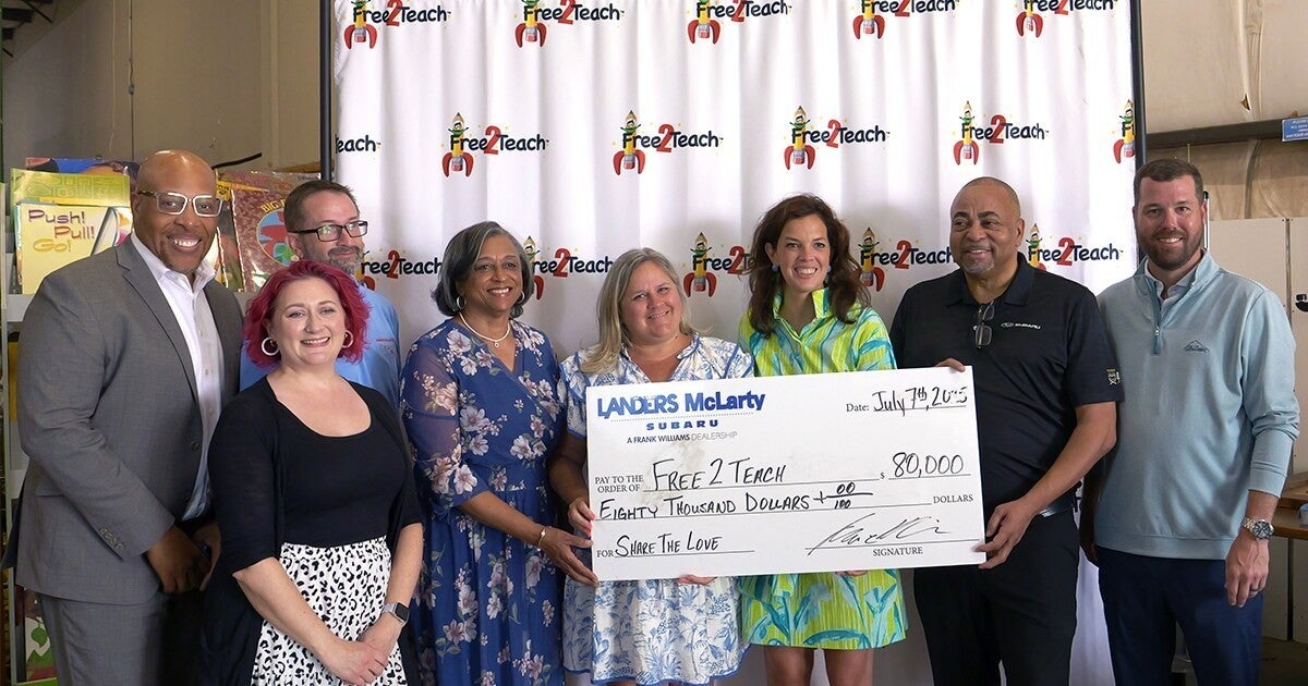 Nine people pose with an oversized check for $80,000 from Landers McLarty Subaru to Free 2 Teach