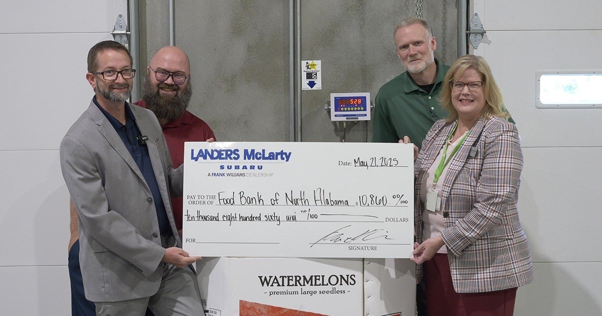 Four smiling people holding a large check for $10,860 from Landers McLarty Subaru to the Food Bank of North Alabama