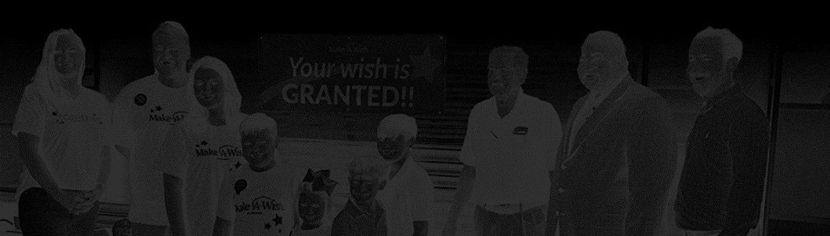 A very dark photo shows 8-10 people, including children, in front of a Your wish is GRANTED!! Make-A-Wish sign