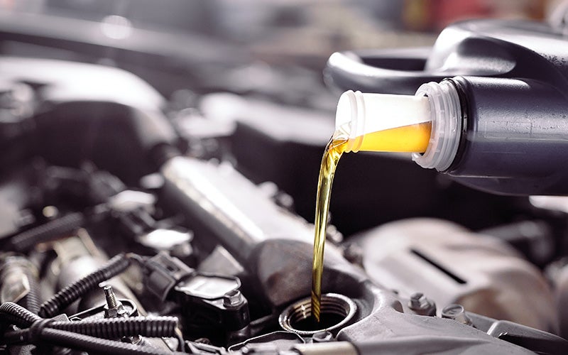 Motor oil being poured from a container into the engine oil fill opening of a vehicle during routine maintenance